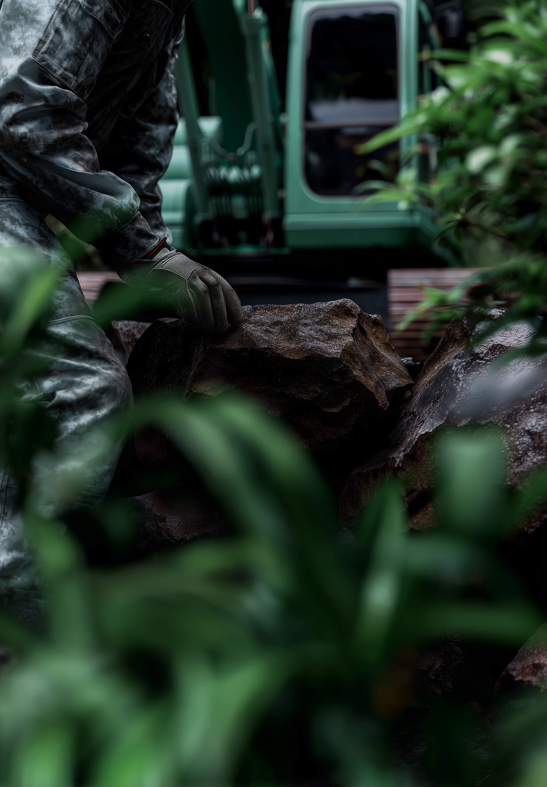Landschaftsgärtner platziert Naturstein, im Hintergrund ein Bagger – Bau von Gartenanlagen